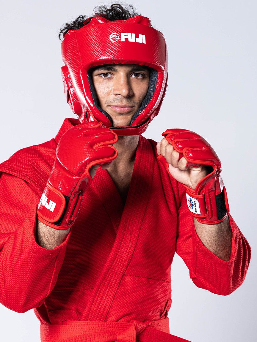A person wearing a red martial arts uniform, protective headgear, and red FIAS Sambo Combat Gloves, holding their hands in a fighting stance.