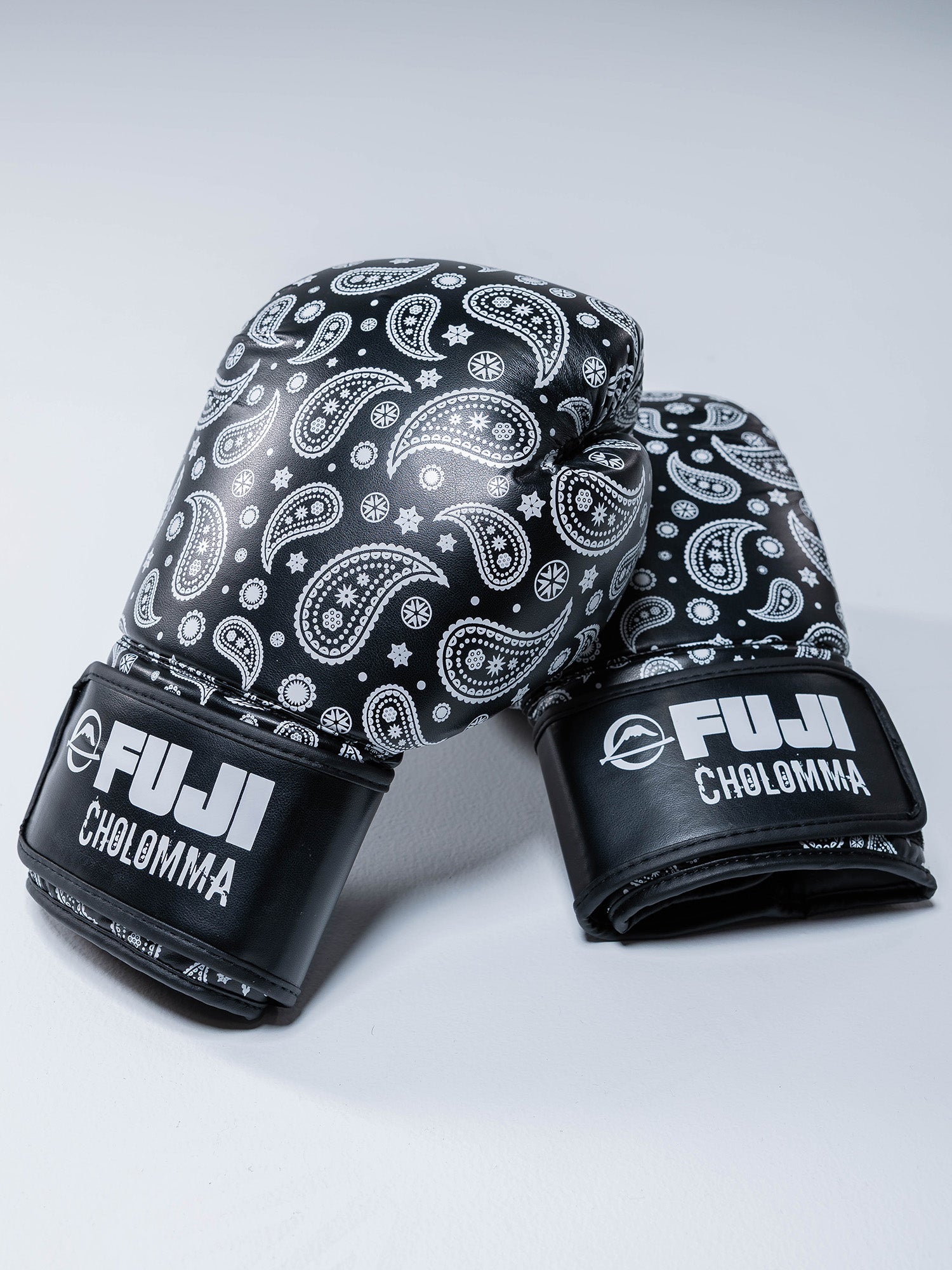 A pair of black CholoMMA Paisley 16oz Boxing Gloves with white paisley designs and FUJI and CHOLOMMA logos on the wrist straps, displayed on a light surface.