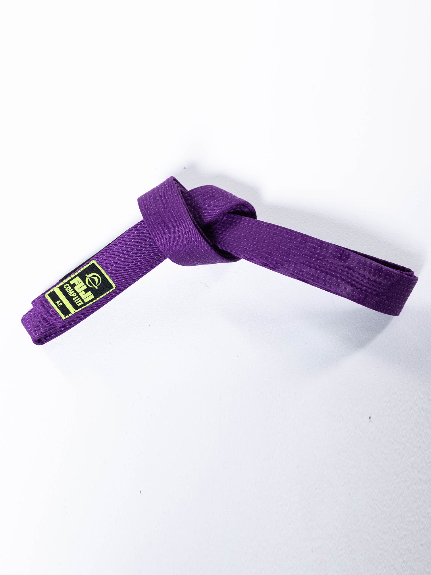 The BJJ Comp Lite Belt Purple, featuring a black and yellow patch, is shown knotted against a white background.