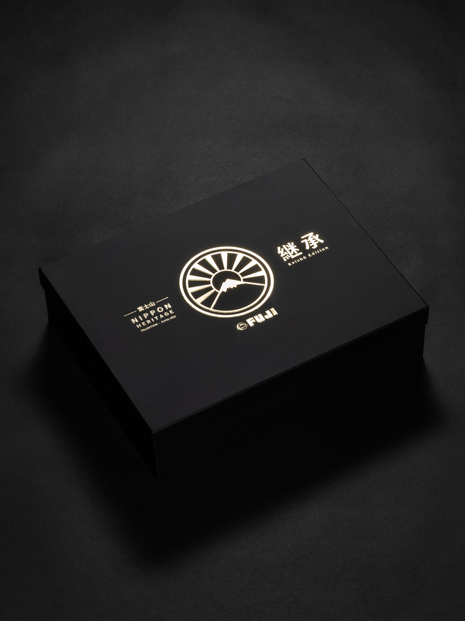 A black Womens Heritage Keisho Lightweight BJJ Gi box featuring gold Japanese text, a stylized sunrise logo, and the word FUJI on the lid, placed on a dark surface.