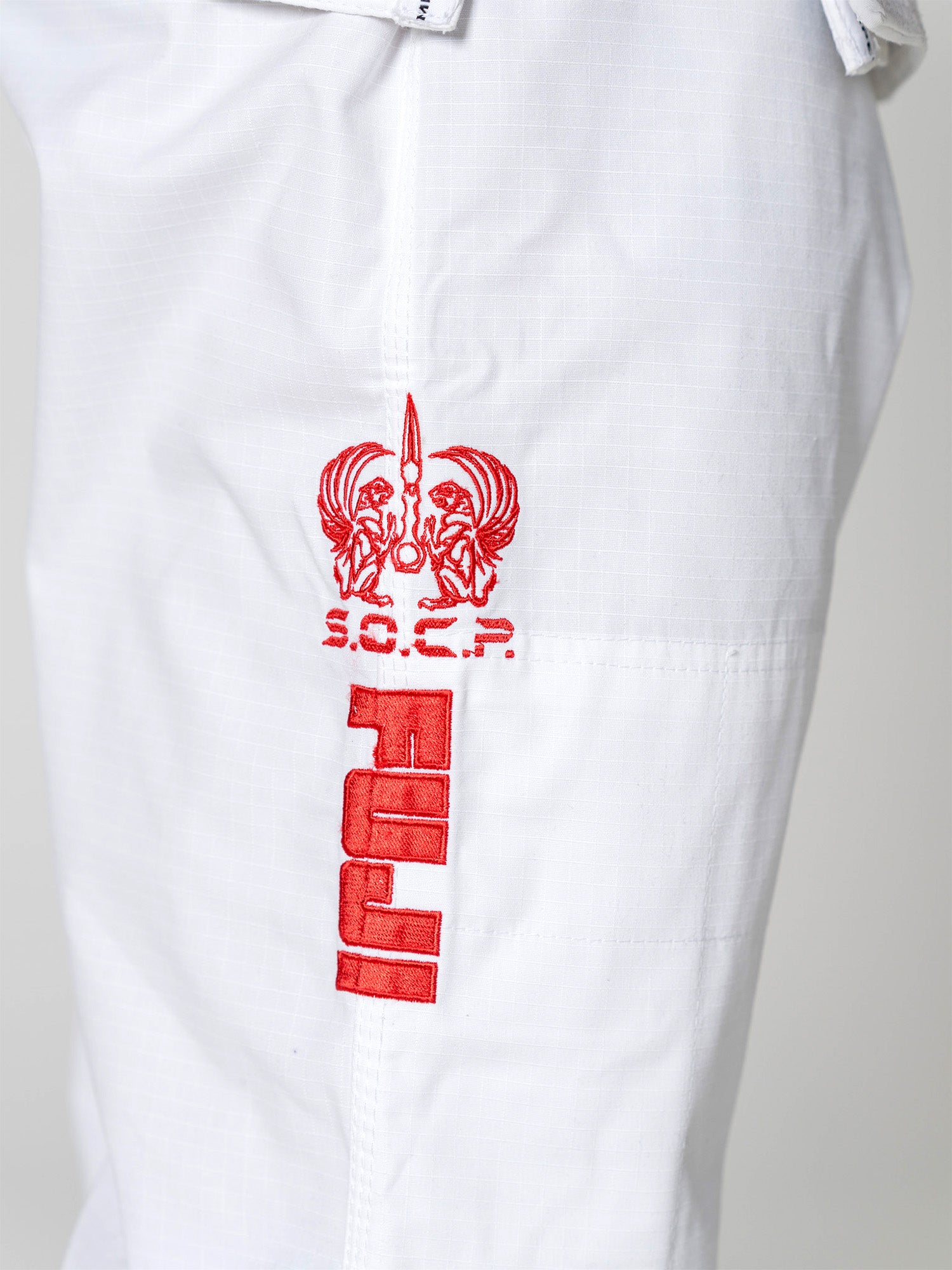 Close-up of the S.O.C.P. Sekai BJJ Gi 2.0 White pants, featuring a red embroidered S.O.C.P. logo and stylized emblem above bold, vertical red JIU text.