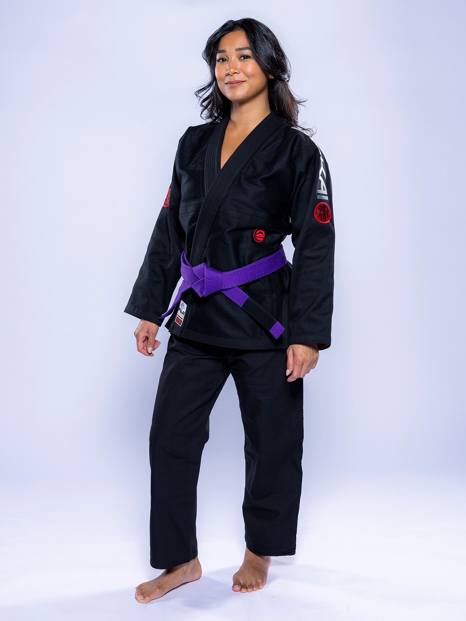 A woman stands barefoot on a white background, confidently wearing the Womens SEKAI 3.0 BJJ Gi Black Grey with a purple belt. She looks at the camera with a slight smile and a relaxed posture.