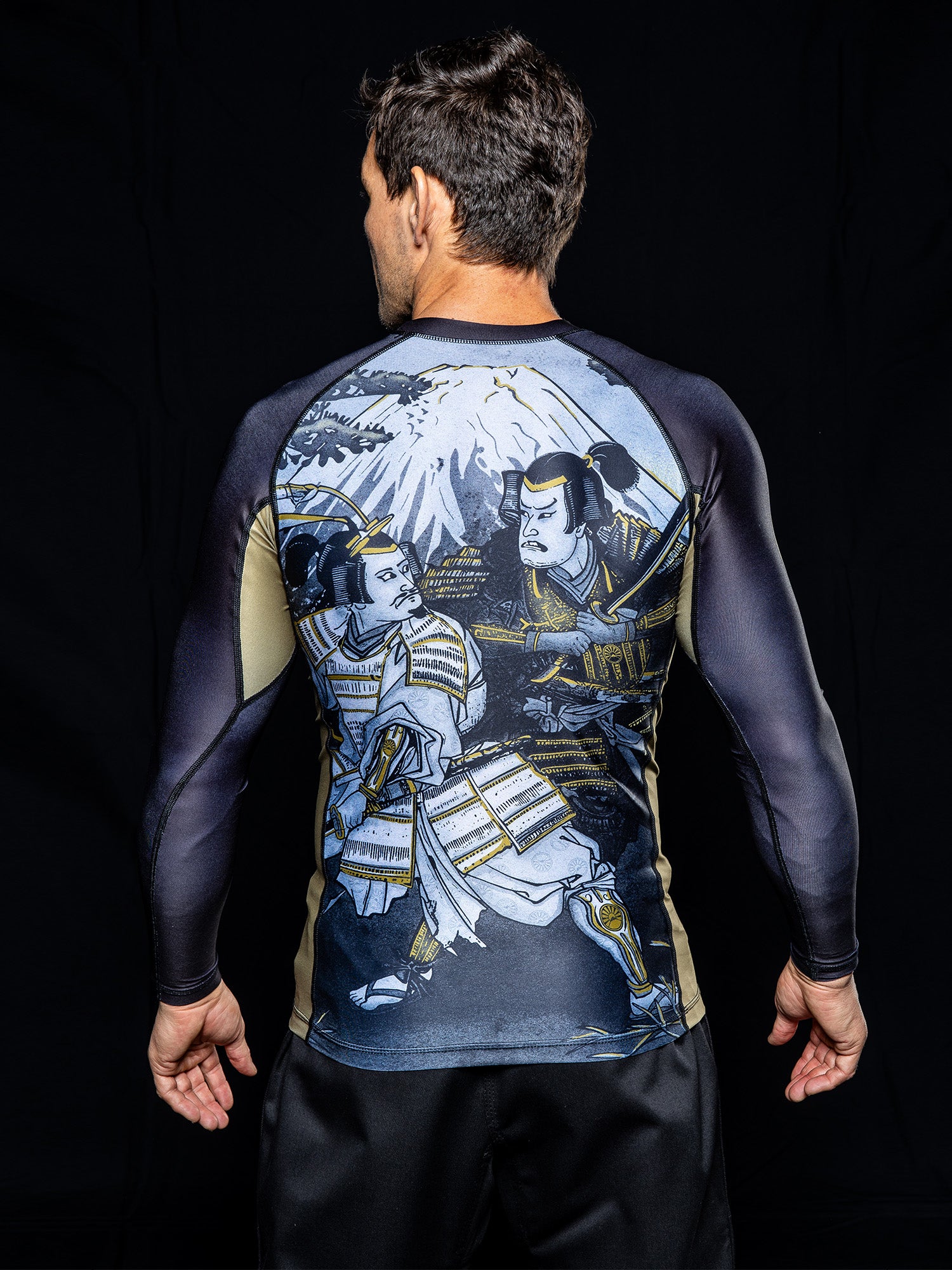 A man stands with his back to the camera, wearing a long-sleeve shirt from the Heritage Keishō Edition Bundle, which features a samurai-themed design with two samurai and a mountain in the background.