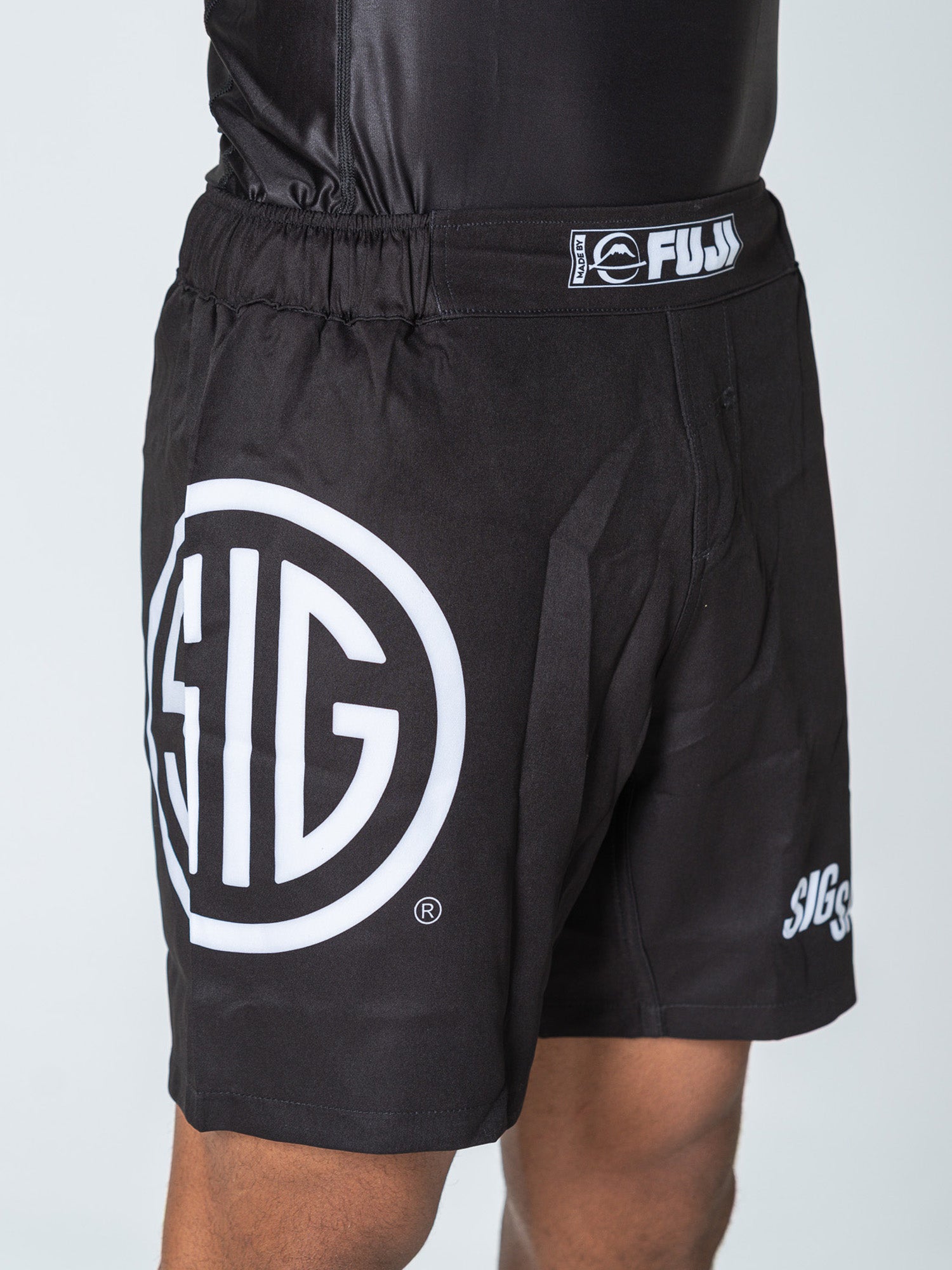 A person wearing Sig Sauer Lightweight Shorts Black, featuring a large white SIG logo on the left thigh and a FUJI label on the waistband; only the lower torso and upper legs are visible in the cropped image.