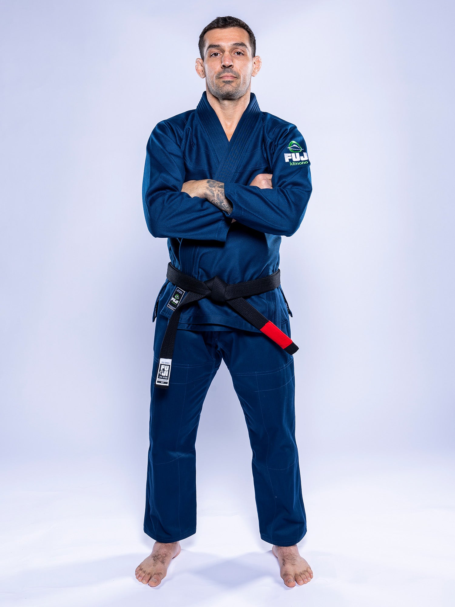 A man wears the Lightweight BJJ Gi Navy with a black belt, standing barefoot and confidently with arms crossed against a light background.