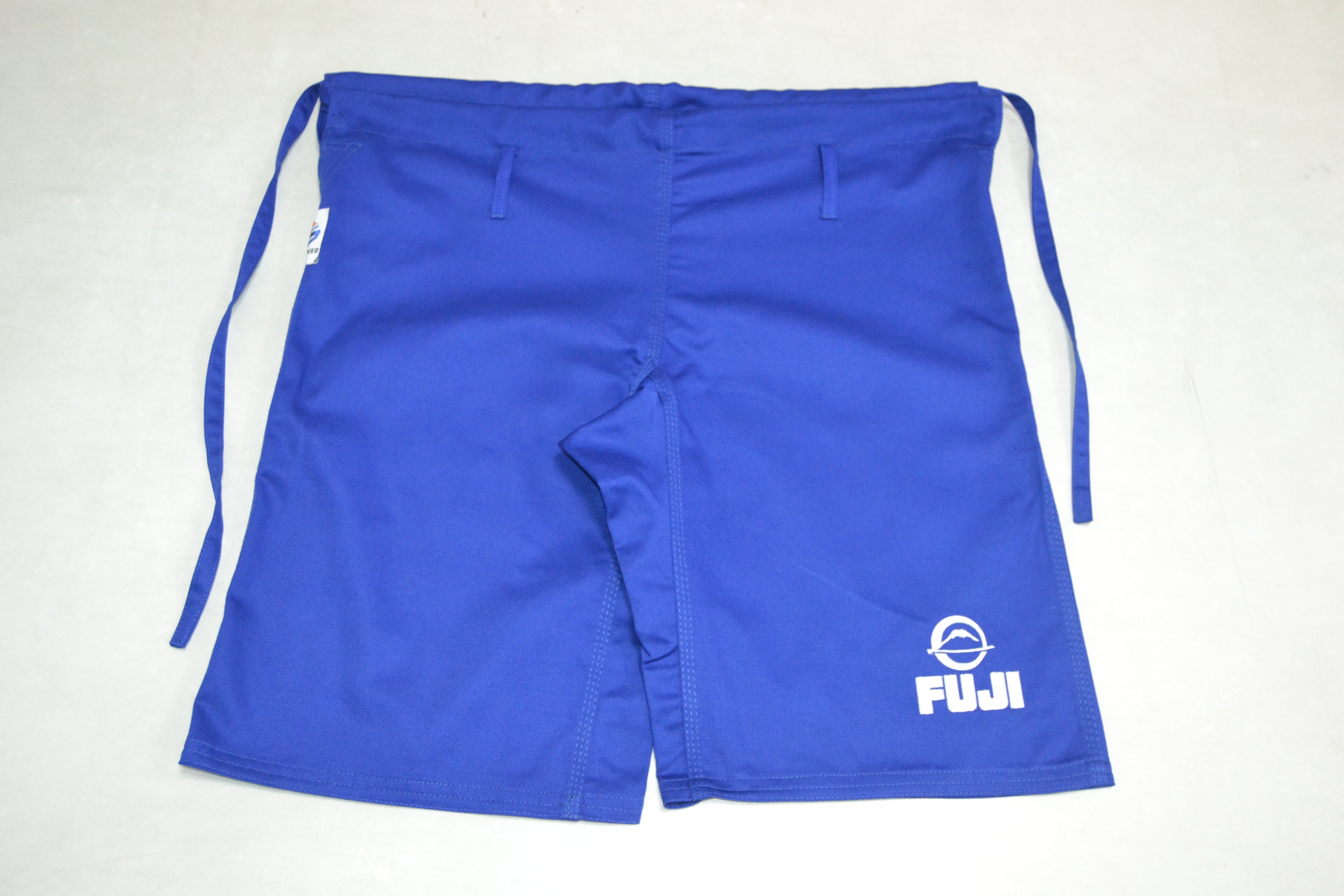 FIAS Combat Sambo Shorts Blue featuring FUJI and a circular logo printed in white on the left leg. These bright blue athletic shorts have two side drawstrings and belt loops, and are laid flat on a light surface.