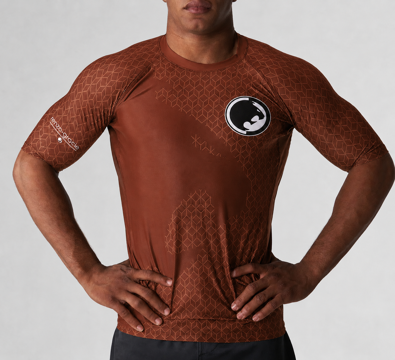 A person wearing the Renzo Gracie Mecca Ranked Short Sleeve Rashguard with geometric patterns and a circular chest logo stands with hands on hips against a plain background.