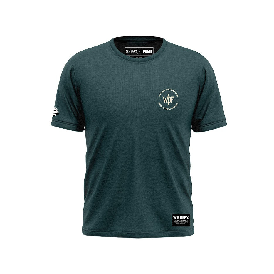 The We Defy Monogram T-Shirt Green features short sleeves, a dark green color, the WE DEFY FOUNDATION text with a circular logo on the left chest, a white logo on the right sleeve, and a WE DEFY label at the bottom front. Displayed on white background.