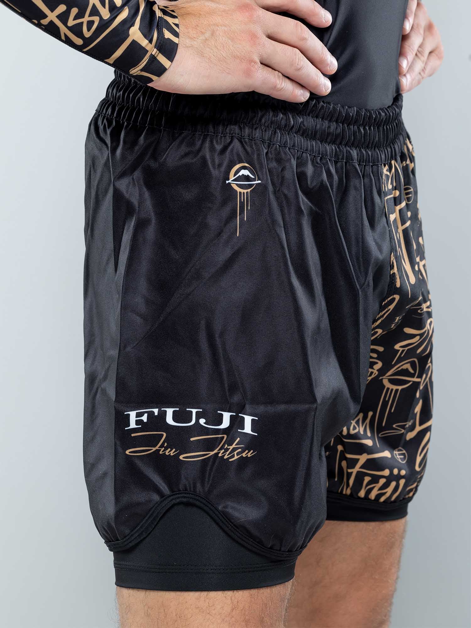 A person wearing Shinobi Fight Shorts Black With Liner featuring gold lettering and a stylized logo, plus a matching black and gold rash guard, stands with hands on hips.