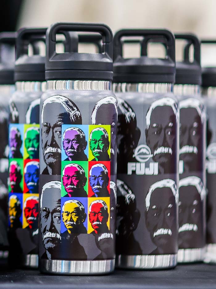 Kano Tumbler 26oz, a metal water bottle with a black lid and a pop-art style repeating portrait print in colorful squares.