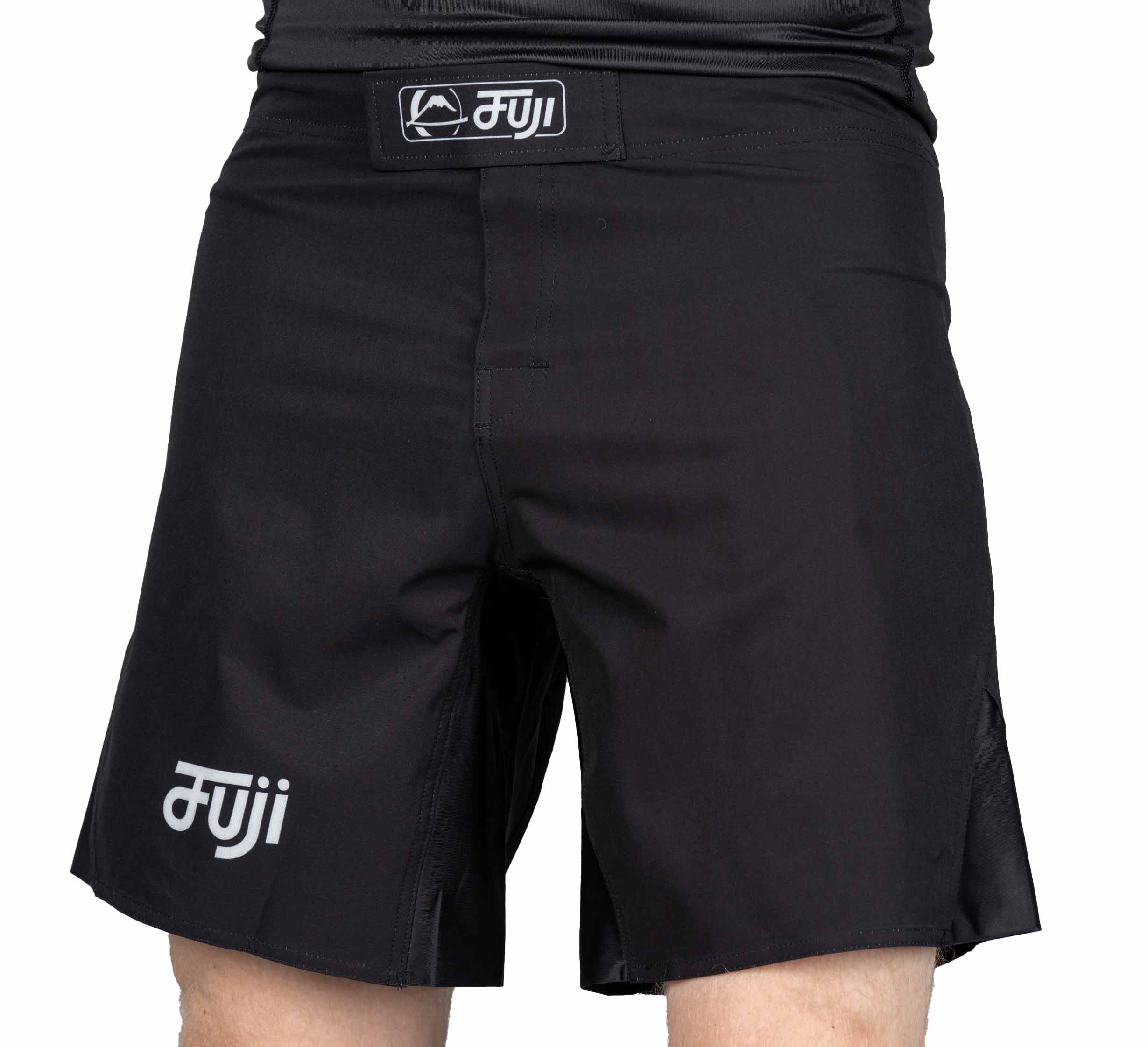 Someone wearing black Pro-Tech Grappling Fight Shorts with a front Velcro closure and white Fuji logos on the waistband and left leg. The shorts are mid-thigh length.